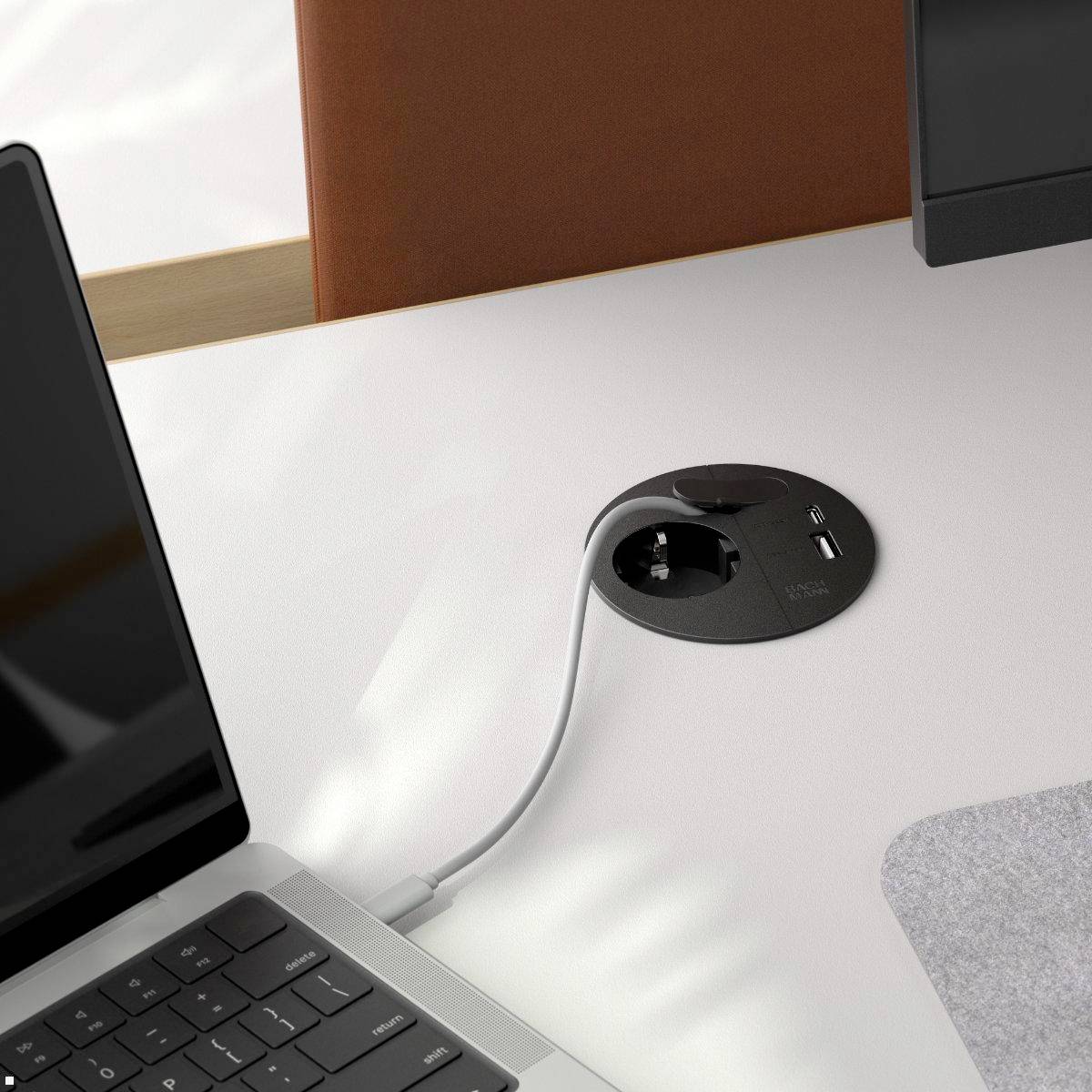 Ein Ladekabel, das in eine Schreibtischsteckdose in der Nähe eines Laptops und einer Tasse gesteckt ist und eine moderne, organisierte Arbeitsumgebung andeutet.