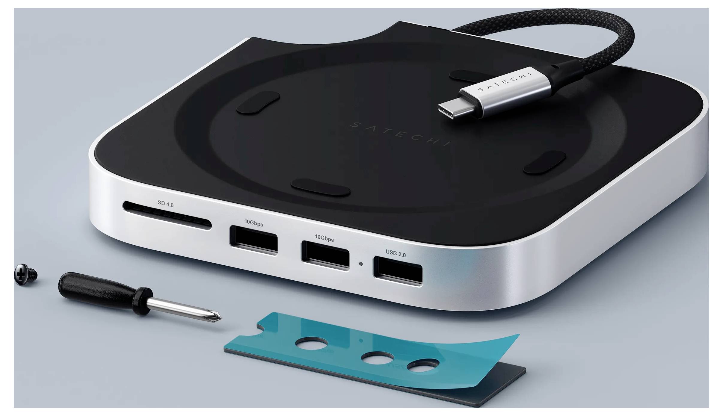Ein schlanker USB-C-Hub mit mehreren Anschlüssen für HDMI und USB-Verbindungen, begleitet von einem Schraubendreher und einem petrolblauen Streifen auf einer grauen Oberfläche.