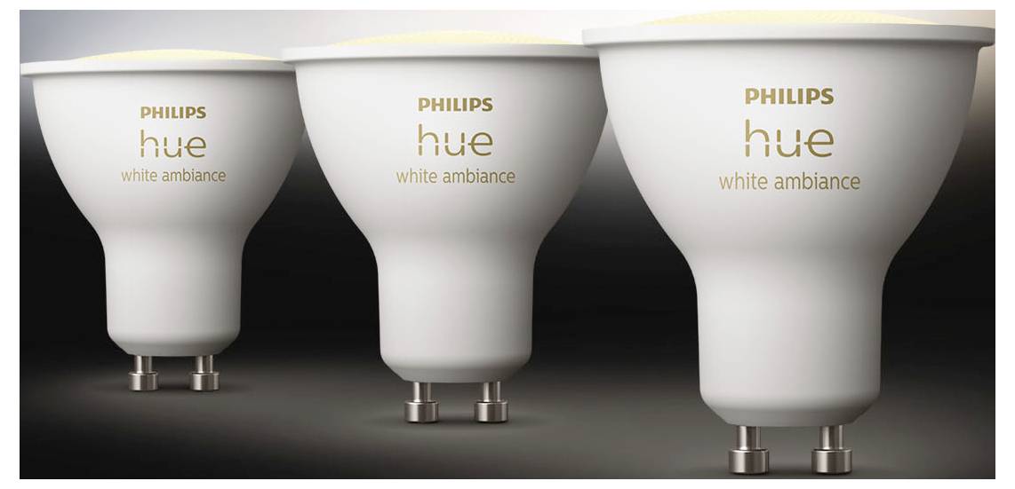 Drei Philips Hue White Ambiance LED-Lampen mit GU10-Sockel, von links nach rechts ausgerichtet vor einem Farbverlaufshintergrund in Grautönen.