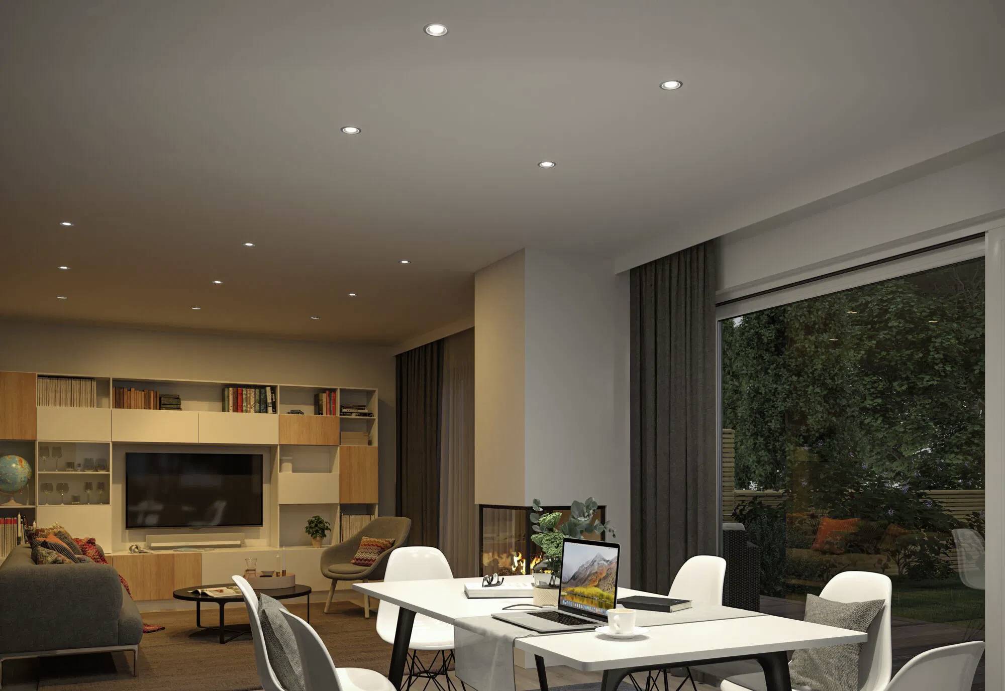 Ein modernes Wohnzimmer mit Essbereich. Zu den Merkmalen gehören ein langer Tisch mit Stühlen, ein Sofa, Bücherregale und ein großes Fenster mit Blick auf einen Garten.