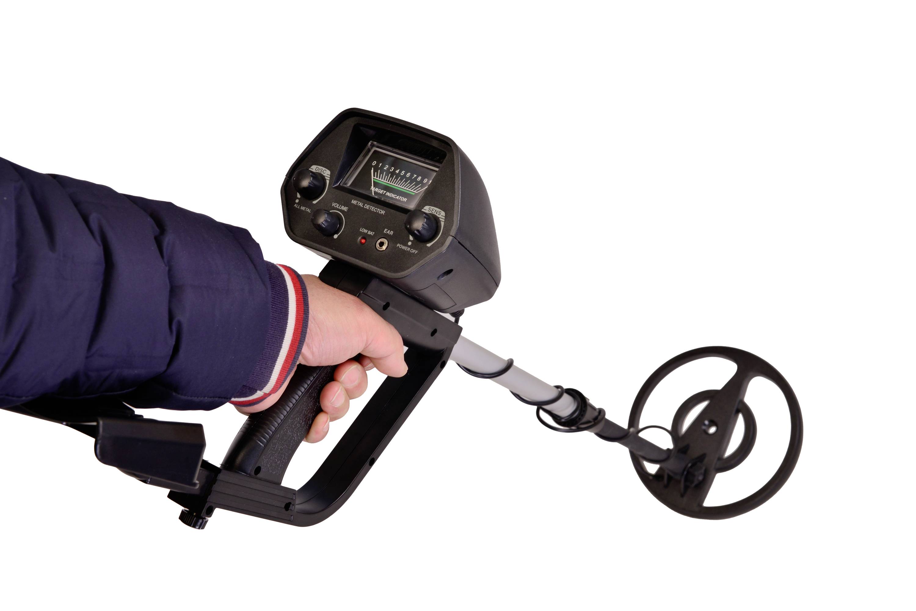 Eine Person hält einen Metalldetektor und richtet dessen kreisförmige Spule zum Boden. Das Gerät verfügt über ein Bedienfeld mit einem Bildschirm und Tasten.