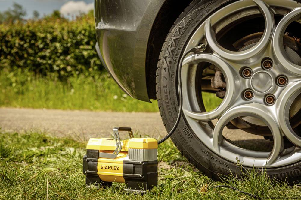 Ein tragbarer Luftkompressor, der an einem Autoreifen an einem sonnigen Tag angeschlossen ist und die Reifenaufpumpen in einer grasbewachsenen Außenumgebung demonstriert.