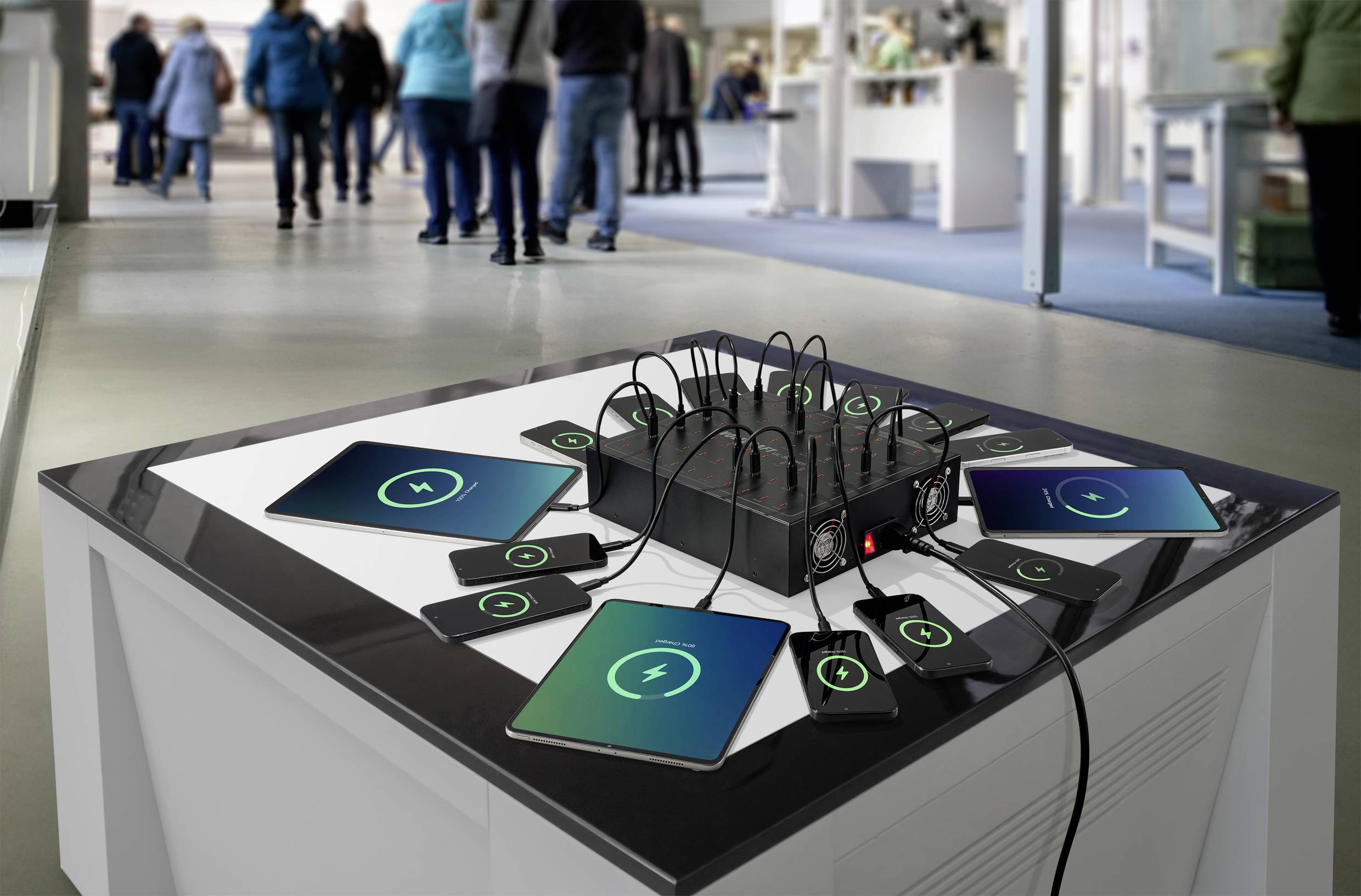 Mehrere Geräte, einschließlich Tablets und Smartphones, sind mit einem zentralen Ladehub auf einem Tisch in einer Technologiegeschäftsumgebung verbunden.