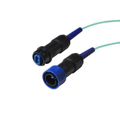 Nahaufnahme von zwei Glasfaserverbindern mit blauer Abdeckung, die durch ein grünes Kabel verbunden sind und für die Datenübertragung in Netzwerken verwendet werden.