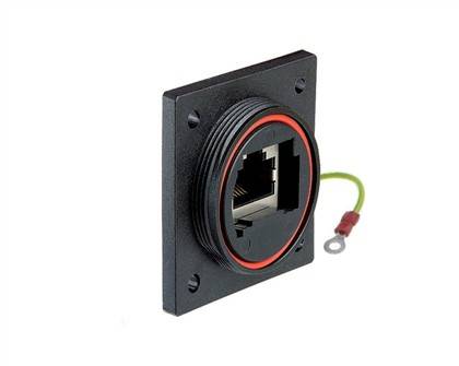 Ein quadratischer schwarzer RJ45-Ethernet-Stecker mit einem roten kreisförmigen Siegel, das auf einer Platte montiert ist und einen grünen Erdungsdraht aufweist.