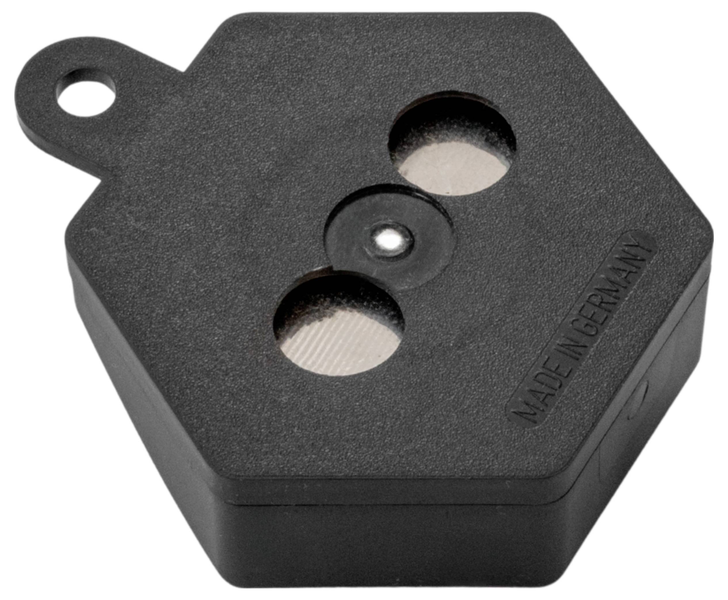 Ein kleines, sechseckiges schwarzes Gerät mit zwei kreisrunden Öffnungen und einer Schlaufe, mit der Aufschrift 