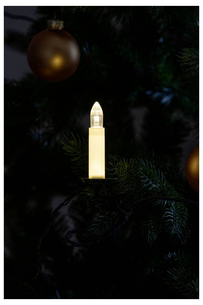 Eine kerzenförmige Lampe leuchtet auf einem geschmückten Weihnachtsbaum, umgeben von dunkelgrünen Zweigen und einigen hängenden Weihnachtsschmuck.