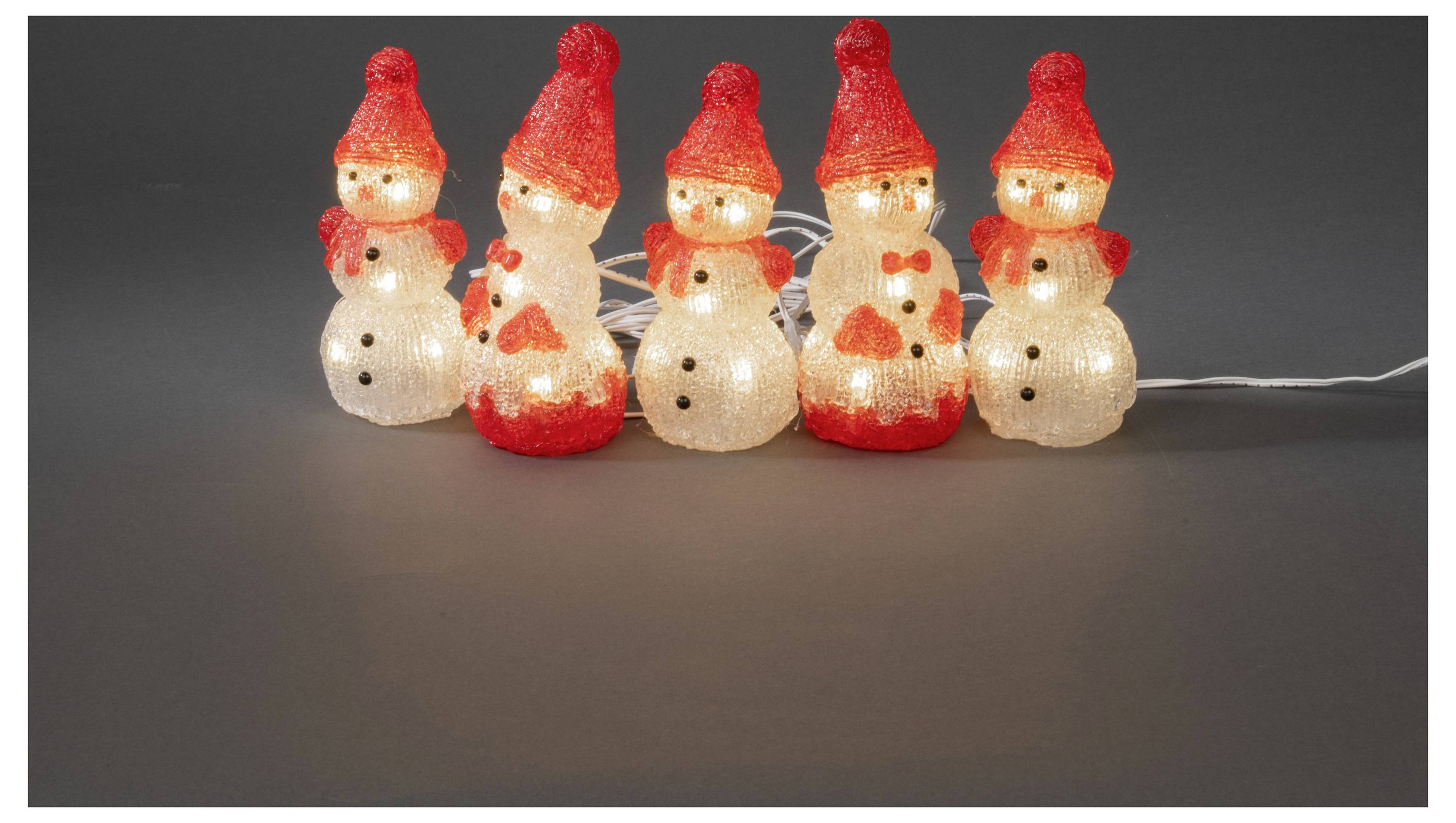 Eine Reihe von fünf beleuchteten Schneemännerdekoration, die jeweils rote Hüte und Schals tragen, auf einer grauen Oberfläche angeordnet.