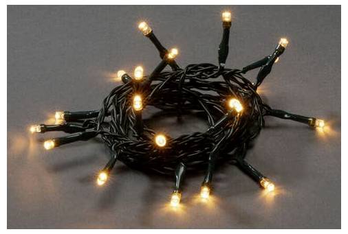 Eine aufgewickelte Kette aus warmweißen LED-Weihnachtslichtern mit schwarzer Verkabelung, die sanft vor einem dunkelgrauen Hintergrund leuchtet.