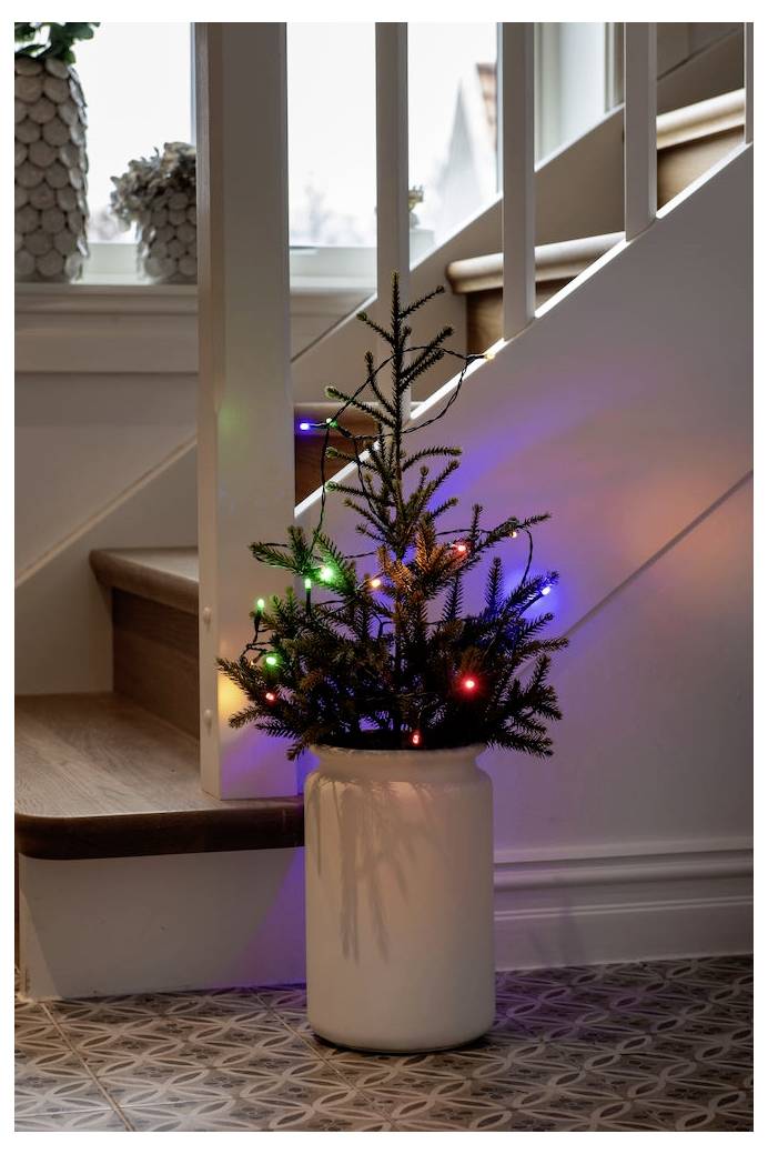 Ein kleiner Weihnachtsbaum mit bunten Lichtern in einem weißen Topf steht auf einem Treppenabsatz und verleiht dem Innenraum festliche Dekoration.