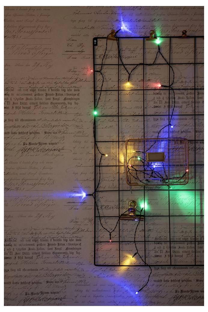 Ein Drahtgitter an einer Wand, geschmückt mit bunten, leuchtenden Lichterketten. Die Wand hat einen Hintergrund im Vintage-Schriftstil.