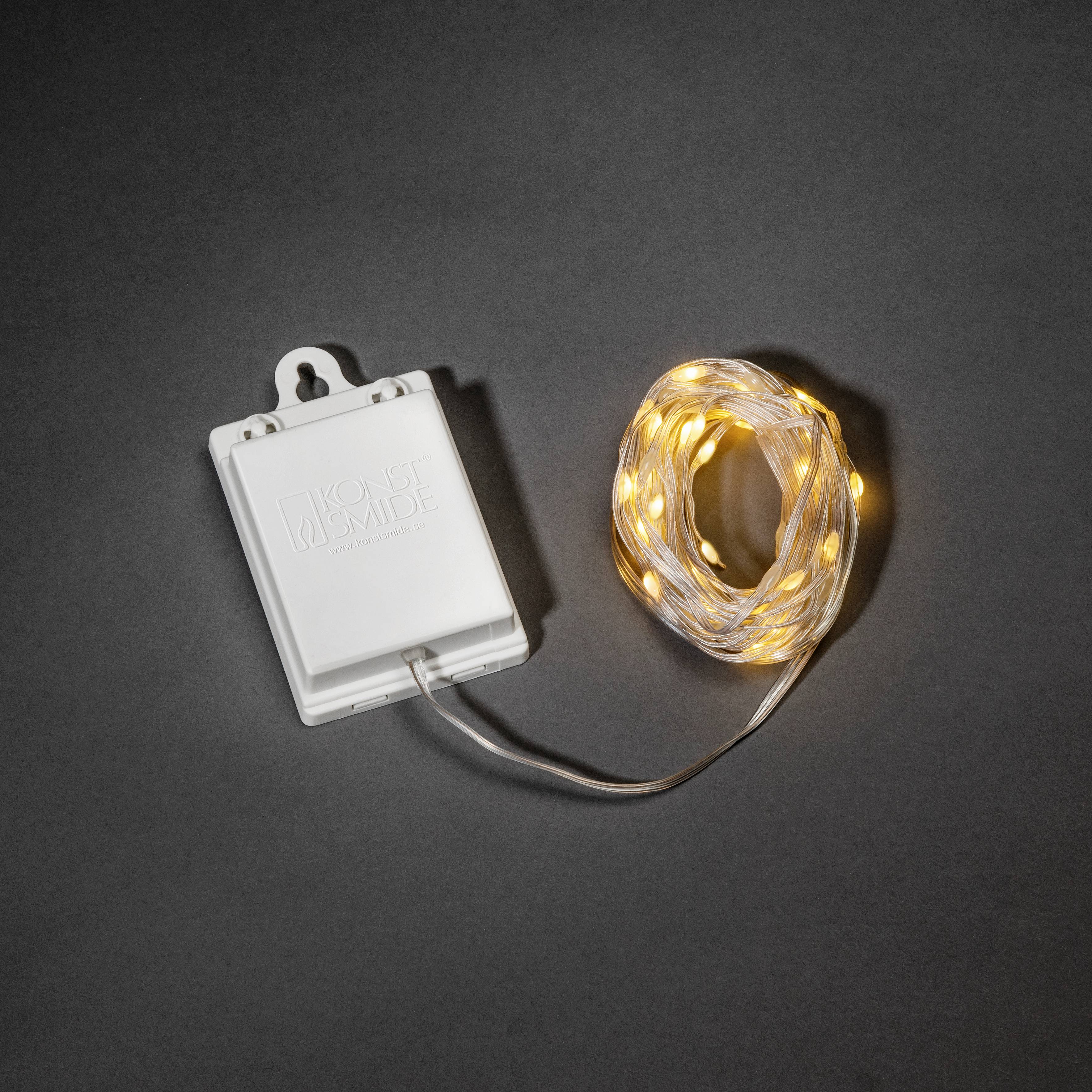Eine aufgewickelte Kette von warmweißen LED-Lichtern, die mit einem Batteriefach verbunden ist und einen sanften Schein ausstrahlt, auf einer dunklen Oberfläche platziert.