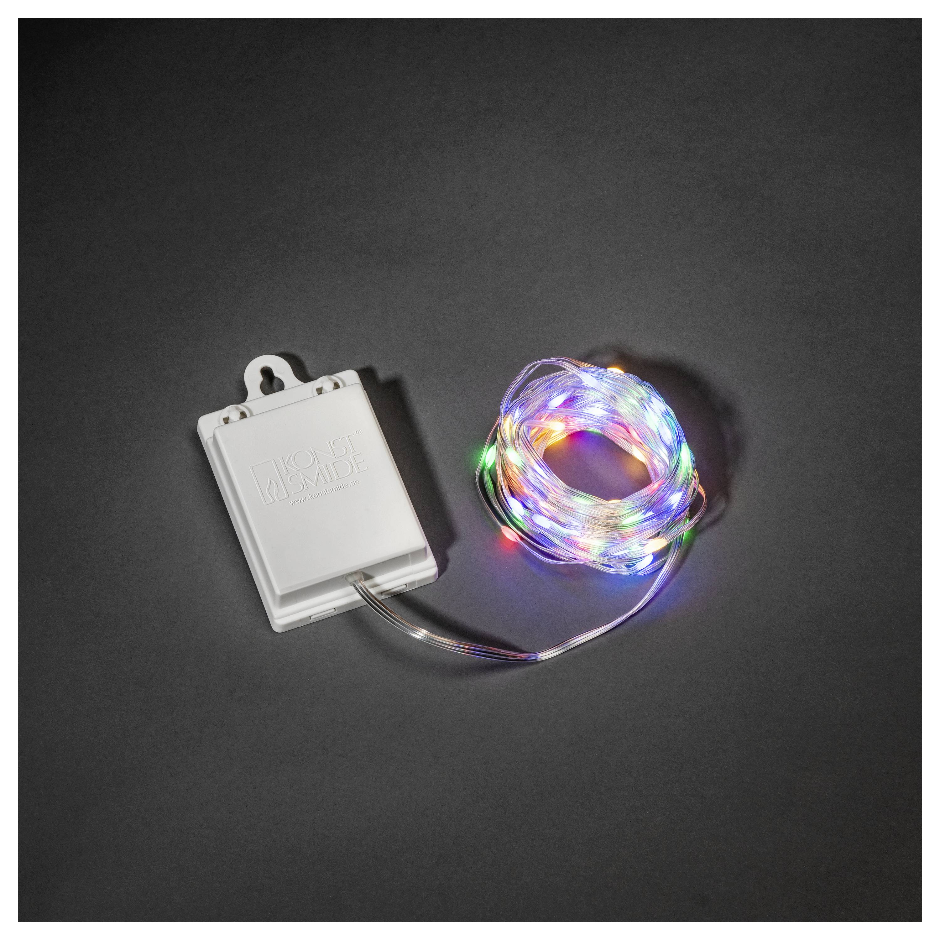 Eine Spule mit mehrfarbigen LED-Lichterketten und einem Batteriefach, die auf einer dunklen Oberfläche platziert ist.