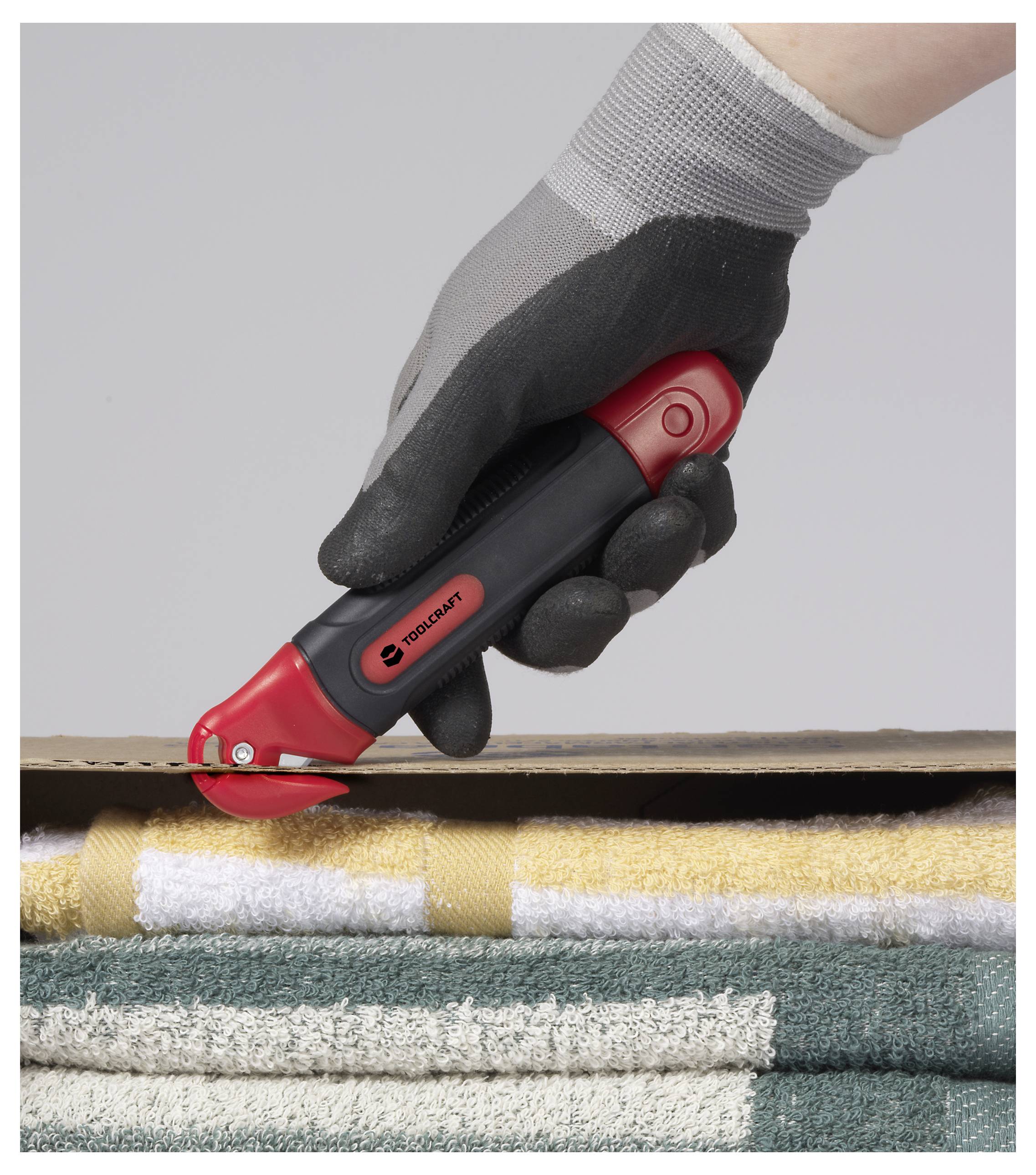 Eine behandschuhte Hand benutzt einen rot-schwarzen Cuttermesser, um durch Karton zu schneiden. Handtücher sind unter dem Karton gestapelt.