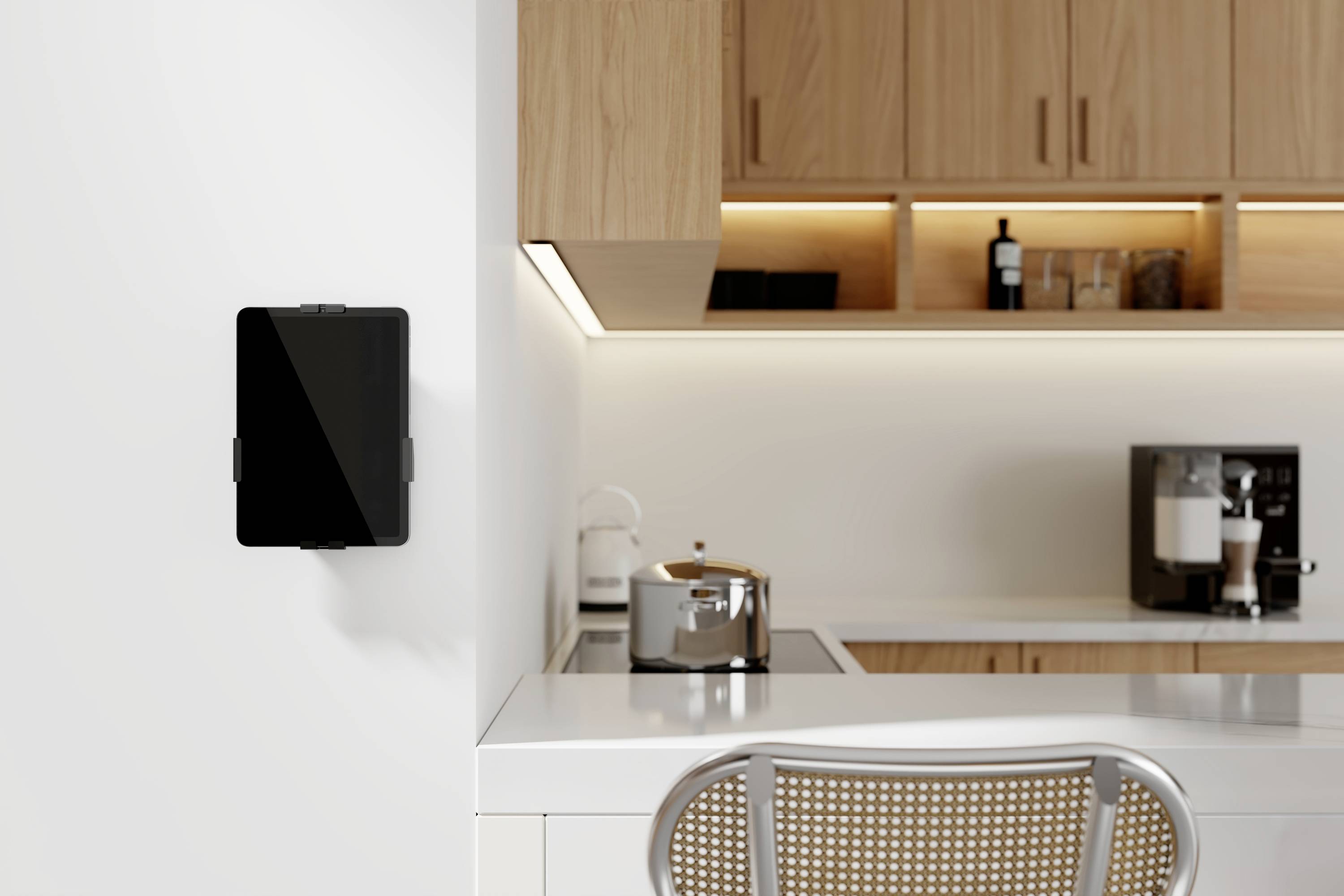 Eine moderne Küche mit hellen Holzschränken, einem an der Wand montierten Tablet, einem Toaster auf der Arbeitsplatte und einer Kaffeemaschine im Hintergrund.