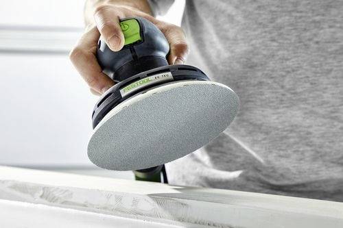 Person mit einer Elektroschleifmaschine auf einer flachen Oberfläche, der Holz oder Putz glättet. Fokus auf dem Schleifpad und der Hand, die das Werkzeug hält.