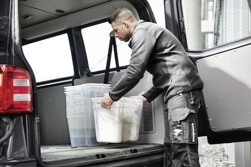 Eine Person, die durchsichtige Plastikbehälter in ein Fahrzeug lädt, möglicherweise beim Organisieren oder Vorbereiten eines Umzugs oder einer Lieferung.