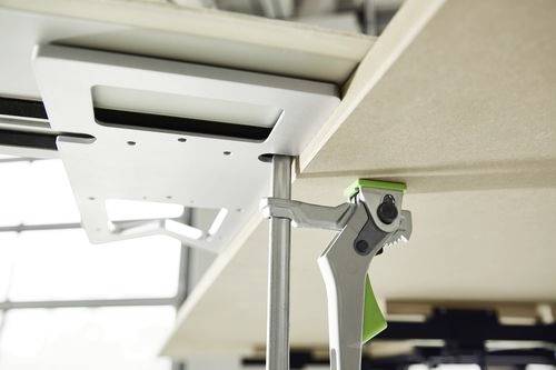 Eine Klemme, die eine Metallhalterung unter einer Holzoberfläche sichert, wahrscheinlich verwendet zum Stabilisieren oder Verbinden von Teilen in der Tischlerei oder beim Möbelaufbau.