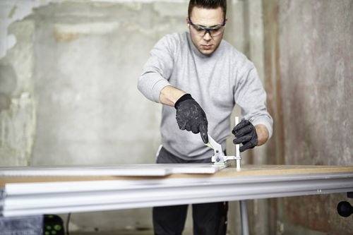 Eine Person mit Schutzbrille und Handschuhen verwendet einen Schneider auf einem Materialstück, aufgenommen in einer industriellen oder Werkstattumgebung.