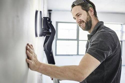 Ein Mann benutzt ein Wandglättungswerkzeug in einem hell erleuchteten Raum und lächelt bei seiner Arbeit.