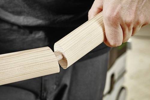 Eine Person verbindet zwei Holzstäbe mit einer Schlitz- und Zapfenverbindung und demonstriert damit eine Holzbearbeitungstechnik.