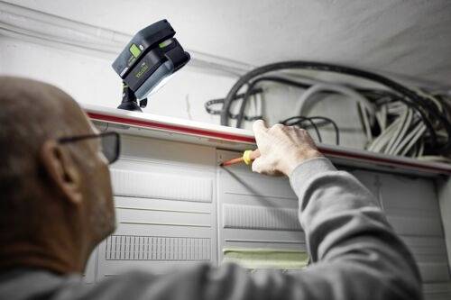 Eine Person verwendet einen Schraubendreher, um an elektrischen Leitungen in einem Schaltschrank zu arbeiten, wobei eine tragbare Arbeitsleuchte den Bereich beleuchtet.