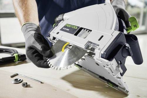 Eine Person mit Handschuhen justiert die Kreissäge einer Festool TS 55 auf einer Holzoberfläche, mit Werkzeugen in der Nähe.