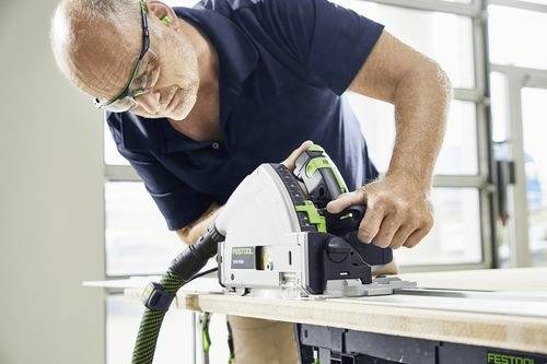 Eine Person mit Schutzbrille verwendet eine tragbare Kreissäge, um Holz an einem Arbeitsplatz zu schneiden und konzentriert sich dabei auf ihre Aufgabe.