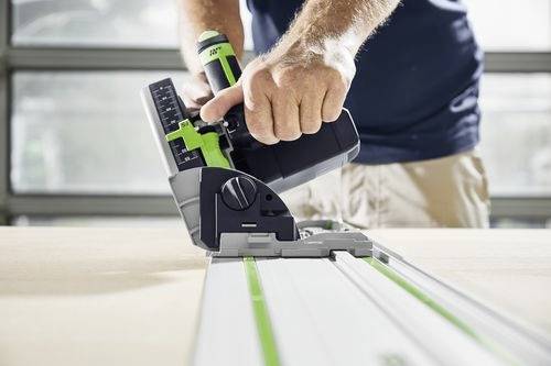 Eine Person bedient eine Kreissäge auf einer Holzoberfläche und konzentriert sich dabei auf präzises Schneiden entlang einer grünen Führungsspur in einer Werkstattumgebung.