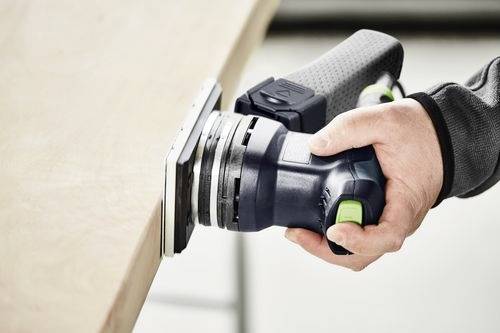 Eine Person verwendet einen tragbaren elektrischen Schleifer auf einer Holzoberfläche und schleift sie gleichmäßig mit Fokus auf Handwerkskunst und Präzision.