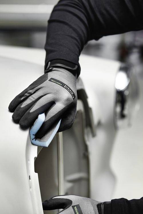 Eine Person mit Handschuhen reinigt eine weiße Autotür mit einem blauen Schwamm und demonstriert dabei Autopflege oder Wartung.