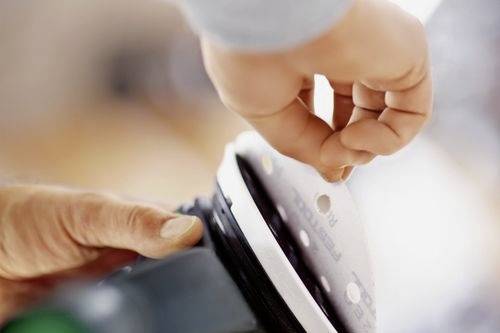 Eine Person befestigt Schleifpapier an einer Elektroschleifmaschine mit einer Hand und konzentriert sich dabei auf das Anbringen der Schleifscheibe an der richtigen Position.