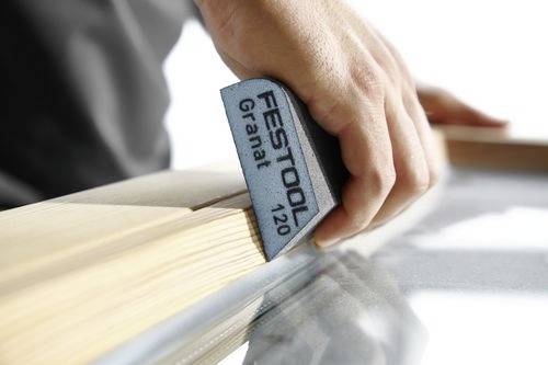 Eine Hand, die eine Holzoberfläche mit einem Festool Granat 120 Schleifklotz schleift und dabei Holzbearbeitung und Oberflächenveredelung betont.