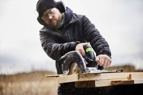 Eine Person in Schutzausrüstung verwendet eine elektrische Säge, um Holzbretter im Freien zu schneiden.