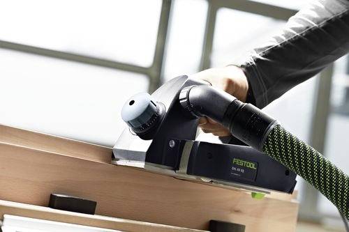 Eine Person verwendet einen Festool-Handhobel, um die Kante eines Holzbretts im Innenbereich zu glätten.