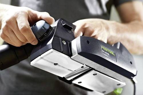 Eine Person, die ein tragbares Elektrowerkzeug einstellt und sich dabei auf einen Zifferblatt mit Markierungen konzentriert. Das Werkzeug scheint für einen präzisen Einsatz bei einem Projekt eingestellt zu werden.