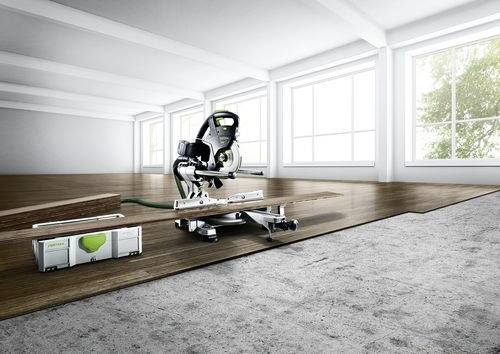 Ein heller, geräumiger Raum ist zu sehen, teilweise renoviert, mit einer Kreissäge auf einem Holzfußbodenabschnitt. Im Vordergrund ist Betonboden sichtbar.