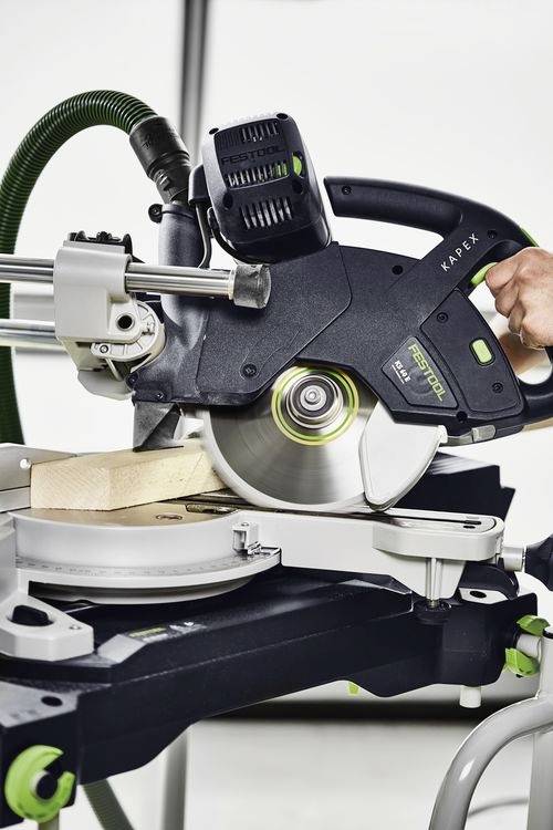 Eine Kapp- und Gehrungssäge, die ein Holzbrett sägt, wobei die Klinge in Bewegung hervorgehoben wird, mit einer Hand, die das Werkzeug für präzises Schneiden einstellt.