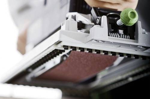 Eine Hand justiert einen grünen Knopf an Büroausrüstung und konzentriert sich auf eine Tonerkartusche oder eine Druckerkomponente, was auf Wartung oder Einrichtung hindeutet.