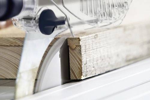 Eine Kreissäge, die durch ein Stück Holz schneidet und Holzbearbeitung oder Zimmermannsarbeit in einem industriellen Umfeld veranschaulicht.