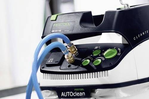 Eine Nahaufnahme eines Festool AUTOClean-Geräts mit zwei blauen Schläuchen, die an Anschlüssen befestigt sind, mit verschiedenen Kontrollknöpfen und einem Tragegriff.