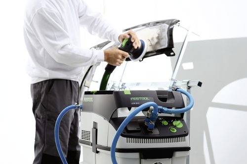 Eine Person verwendet ein Polierwerkzeug, das an einen Festool CTL Mini-Staubsauger angeschlossen ist, höchstwahrscheinlich in einer Autowerkstatt.