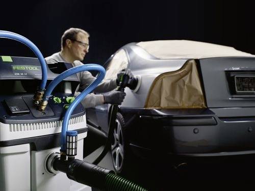 Eine Person poliert ein Auto mit einem Werkzeug, während eine Festool-Maschine in der Nähe angeschlossen ist und einen Autoaufbereitungsprozess andeutet.