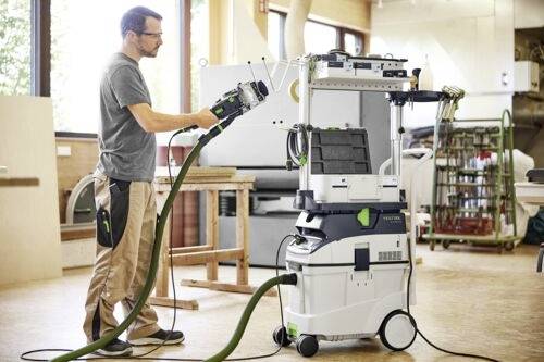 Eine Person, die ein industrielles Vakuumsystem in einer Werkstatt bedient und einen Schlauch an einer fahrbaren Einheit mit Bedienfeld hält.