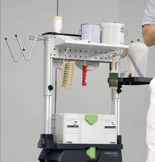 Malstation auf einem Arbeitsrollwagen mit Farbdosen, Pinseln und Werkzeugen. Person teilweise rechts sichtbar.