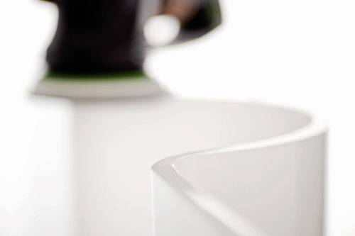 Eine Schleifmaschine nähert sich einer glatten, geschwungenen weißen Oberfläche in einer Nahaufnahme und betont die Präzision und Textur des Materials.