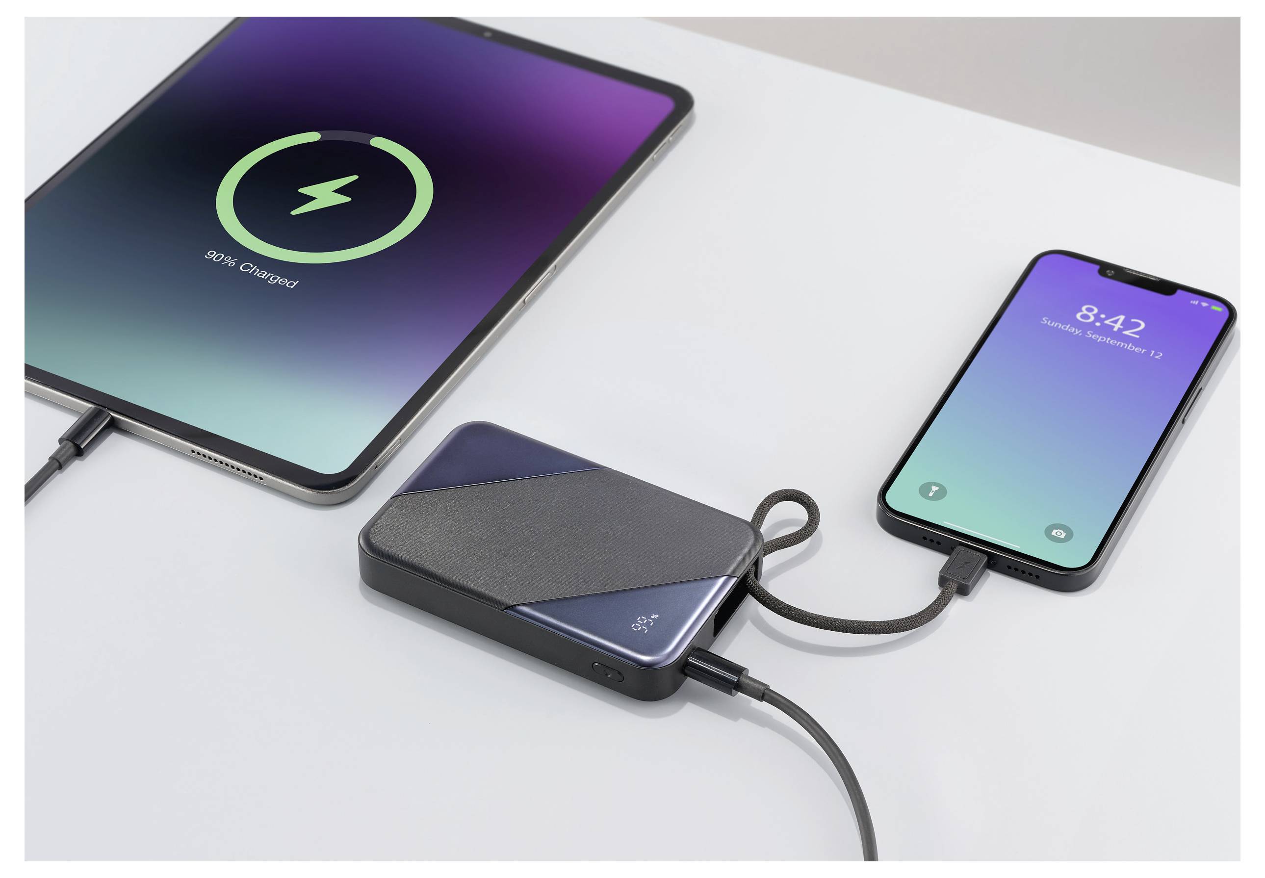 Ein Tablet und ein Smartphone sind mit einem tragbaren Ladegerät auf einem Tisch verbunden. Der Tablet-Bildschirm zeigt „58% aufgeladen