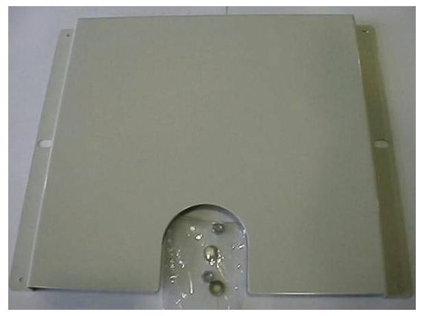 Ein rechteckiges Metallpanel mit einem halbkreisförmigen Ausschnitt am unteren Rand, versehen mit Schrauben und Unterlegscheiben auf einem Kunststoffblatt darunter.