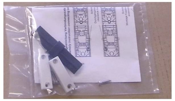Eine Plastiktüte mit Hardwarekomponenten, Schrauben und einem Papier mit Diagrammen auf einer Kartonoberfläche.