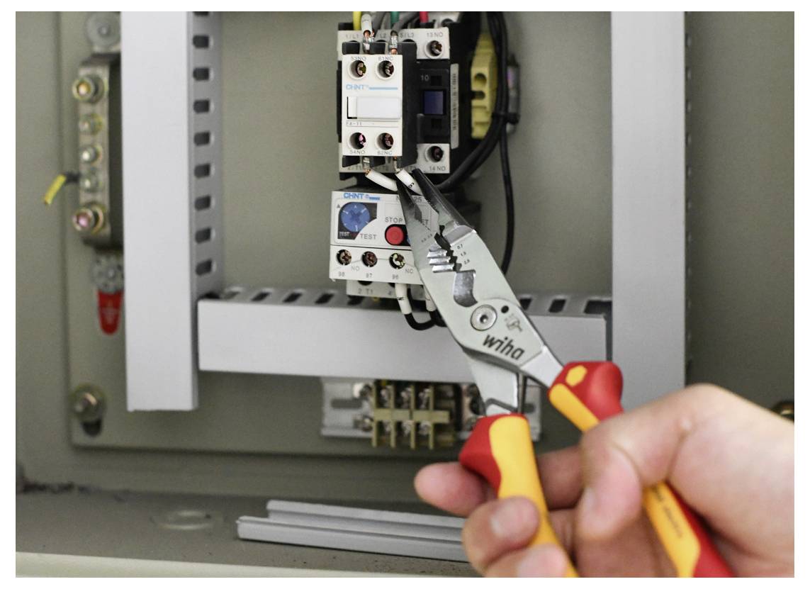 Eine Person verwendet isolierte Zangen, um Drähte in einer elektrischen Sicherungskasten anzupassen und sichere Verbindungen innerhalb einer Schaltanordnung zu gewährleisten.